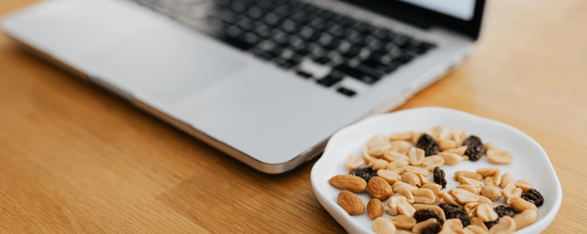 A Laptop on a desk with a bowl of nuts and dried fruit next to it. A Laptop on a desk with a bowl of nuts and dried fruit next to it.