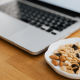 A Laptop on a desk with a bowl of nuts and dried fruit next to it. A Laptop on a desk with a bowl of nuts and dried fruit next to it.