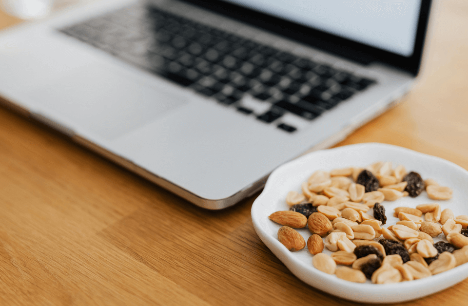 A Laptop on a desk with a bowl of nuts and dried fruit next to it. A Laptop on a desk with a bowl of nuts and dried fruit next to it.