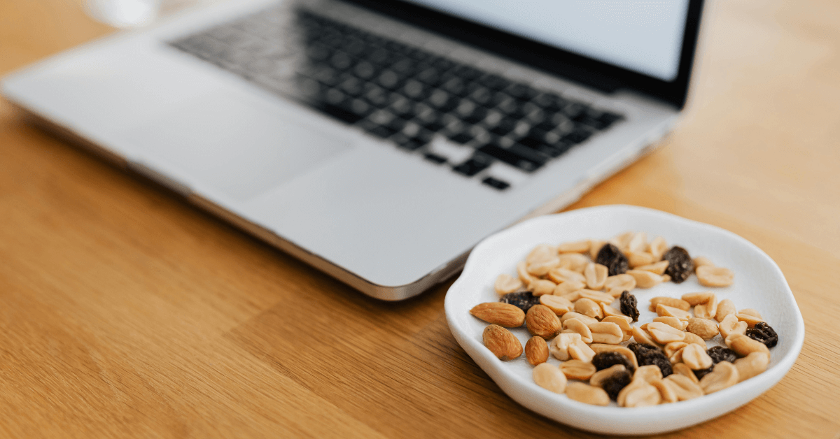 A Laptop on a desk with a bowl of nuts and dried fruit next to it. A Laptop on a desk with a bowl of nuts and dried fruit next to it.